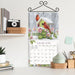 Calendar with a winter scene featuring cardinals and flowers, displayed on a shelf.