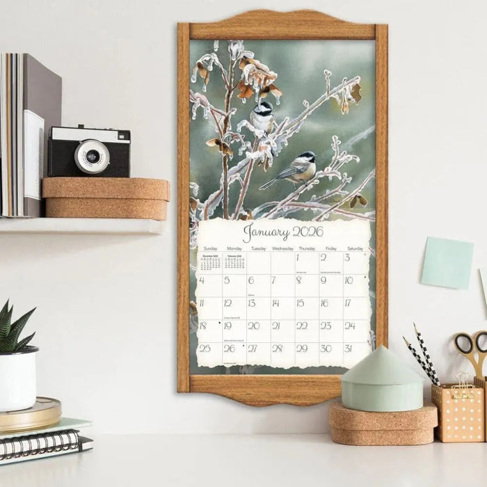 Framed calendar with winter scene and birds on a shelf with decor items.