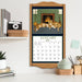 Framed calendar with January 2026 design featuring cats by a fireplace, displayed on a shelf.