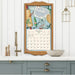 Framed calendar with kitchen-themed design on a white wall above a kitchen counter.