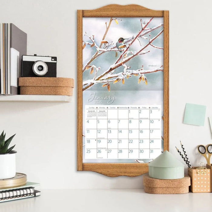Calendar with a winter scene of a bird on a branch, framed in wooden border on a shelf.