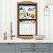 Framed calendar with winter scene design on a wall above a kitchen counter.