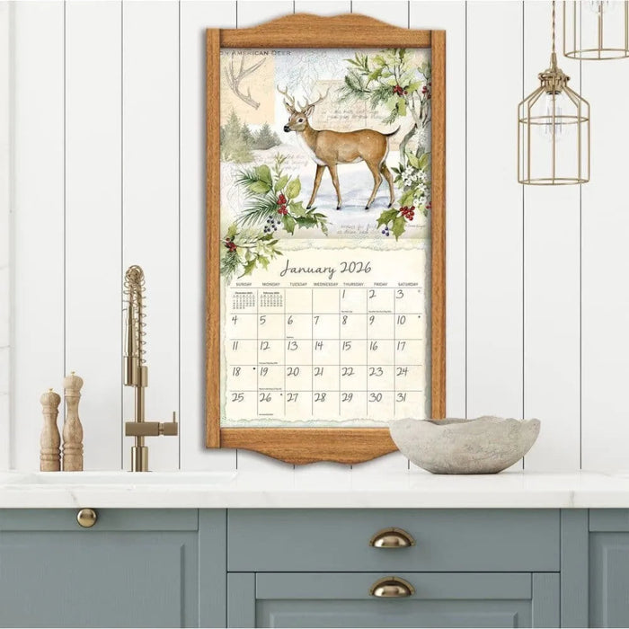 Framed calendar with deer and floral design on a white wall above a shelf.