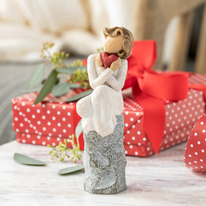 Decorative figurine of a couple holding a heart with wrapped gifts in the background.