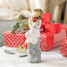 Decorative figurine of a couple holding a heart with wrapped gifts in the background.