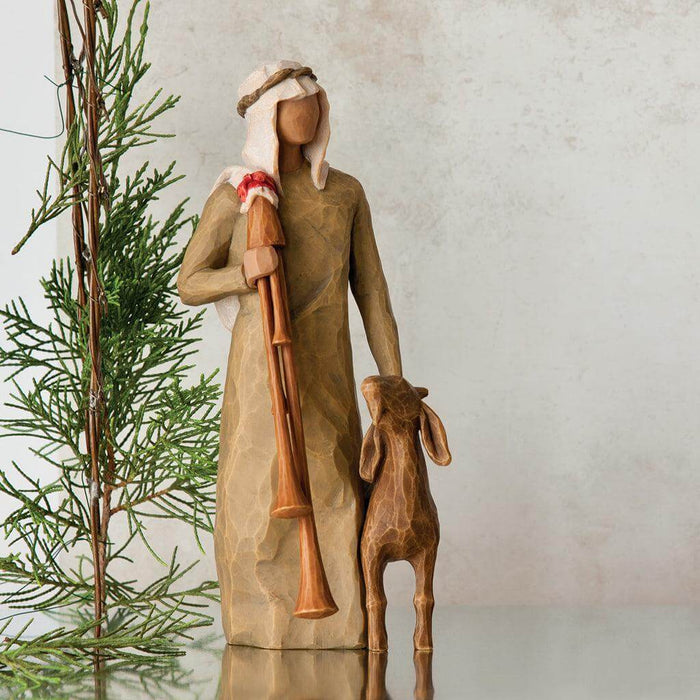 Decorative nativity scene figurine with shepherd and lamb next to a Christmas tree.
