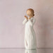 White ceramic figurine of a woman holding a heart-shaped object against a light background