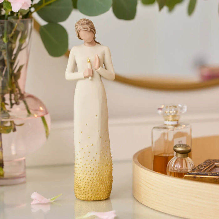 Decorative figurine of a woman holding flowers on a table with a vase and perfume bottles in the background.