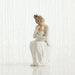 White ceramic figurine of a woman sitting with her hand on her face against a white background