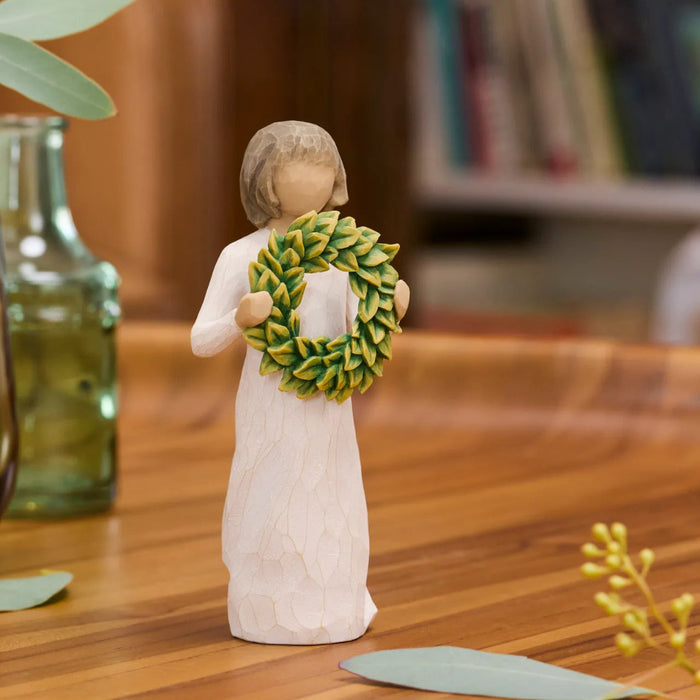Decorative figurine holding a green wreath on a wooden surface.