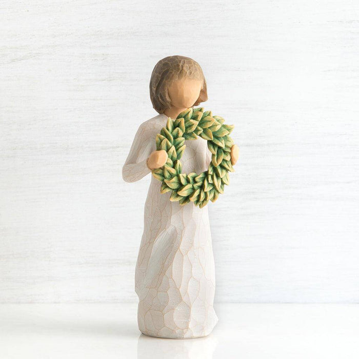 Angel figurine holding a green wreath against a white background