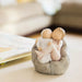 Small figurine of two people sitting together on a rock with a blurred background