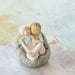 Decorative figurine of two children embracing on a stone base against a soft, multicolored background