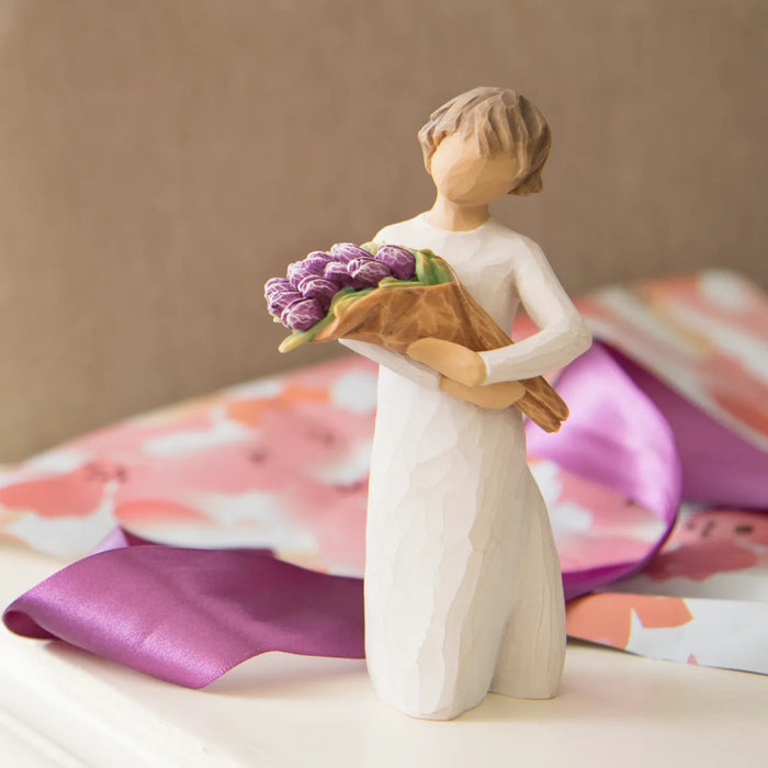 Hand-painted Willow Tree Surprise sculpture with purple bouquet on a table with ribbon and a beige background 