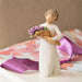 Hand-painted Willow Tree Surprise sculpture with purple bouquet on a table with ribbon and a beige background 