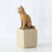 cat figurine on a beige block against a white background