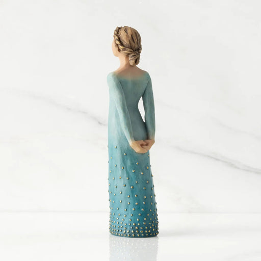 Statue of a woman wearing a long, light blue dress with gold embellishments on a white background
