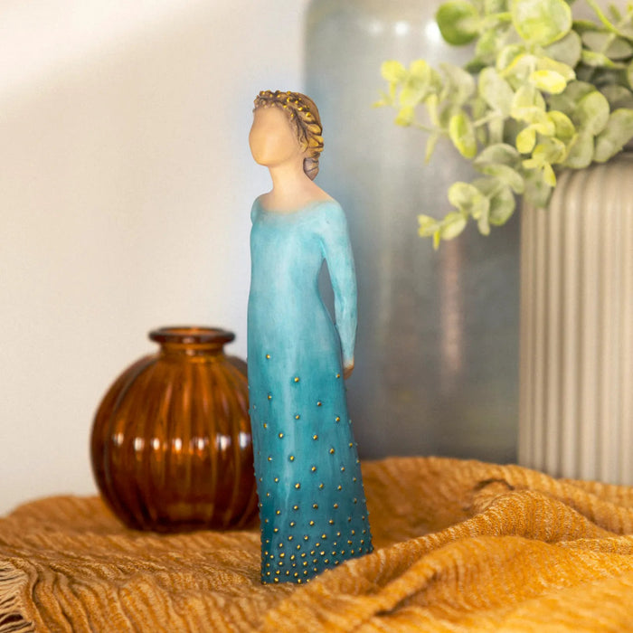 Decorative figurine in a blue dress with gold embellishments on a textured surface.