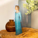 Decorative figurine in a blue dress with gold embellishments on a textured surface.