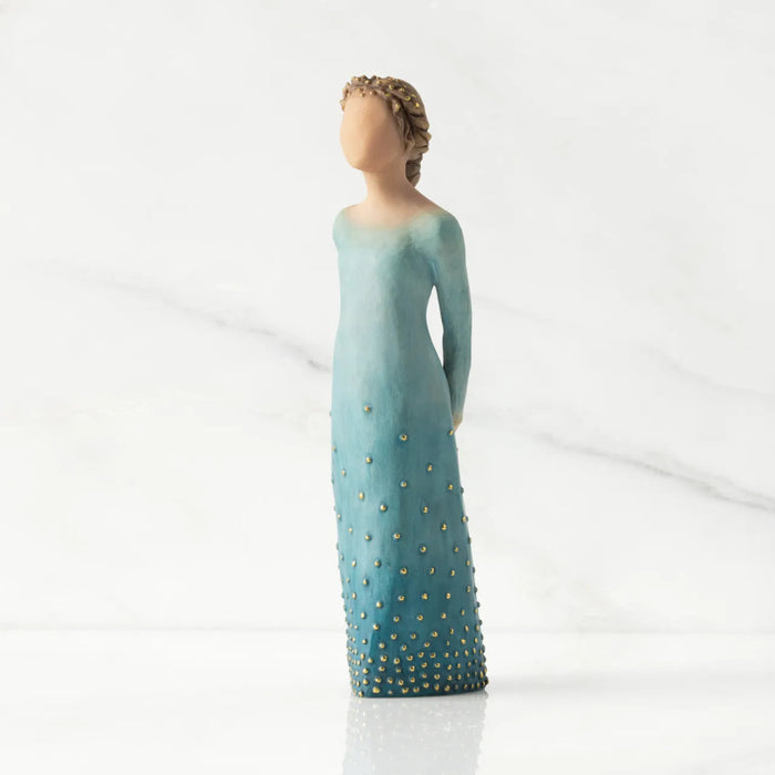 Figurine of a woman in a long, light blue dress with gold accents on a white background