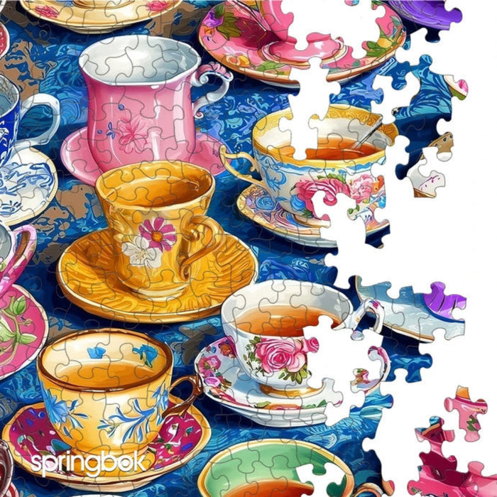 Colorful teacups and saucers on a blue surface with puzzle pieces scattered around, featuring Springbok brand.