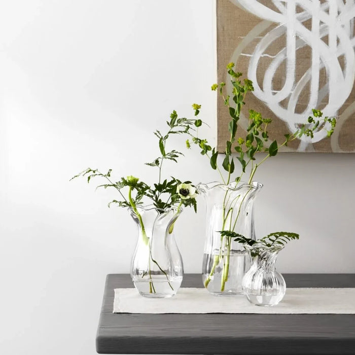 A clear glass vase characterized by a flowing wavy design, emphasizing its stylish and contemporary appearance.