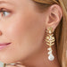A close-up of a woman wearing elegant earrings and a necklace, smiling softly while looking down. 