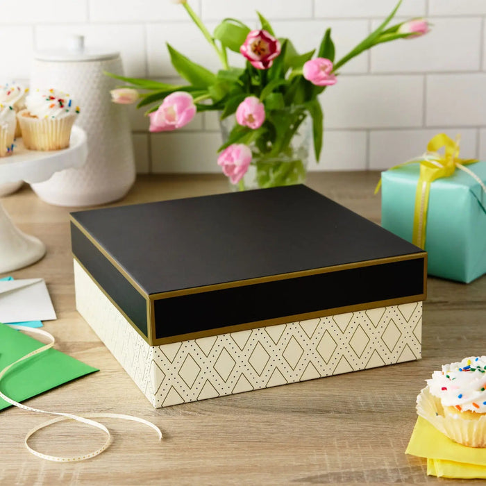 Large white gift box with gold diamond designs and black lid displayed on a party table 