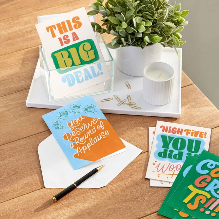 Colorful greeting cards on a wooden surface with a plant and candle.
