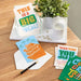 Colorful greeting cards on a wooden surface with a plant and candle.
