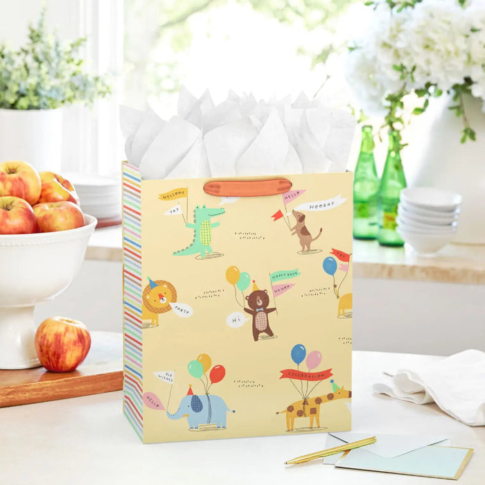 Large yellow gift bag with party‑hat animals and balloons displayed on a table beside a greeting card