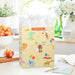 Large yellow gift bag with party‑hat animals and balloons displayed on a table beside a greeting card