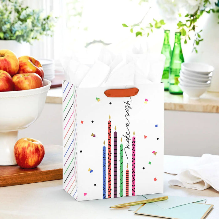 Medium birthday gift bag with colorful candles and gold glitter accents displayed on a table beside a greeting card