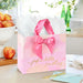 Watercolor‑style pink gift bag with gold‑foil lettering styled on a tabletop with a matching card for birthdays or Mother’s Day