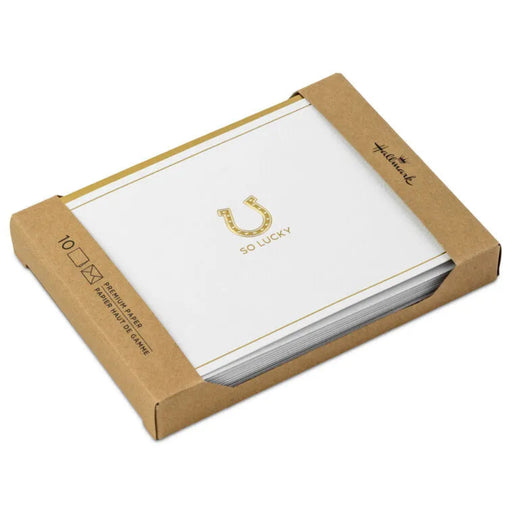 Box of white cards with gold text and a horseshoe symbol on a white background