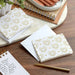 White envelopes with gold patterns on a wooden surface with a pen and notebooks.