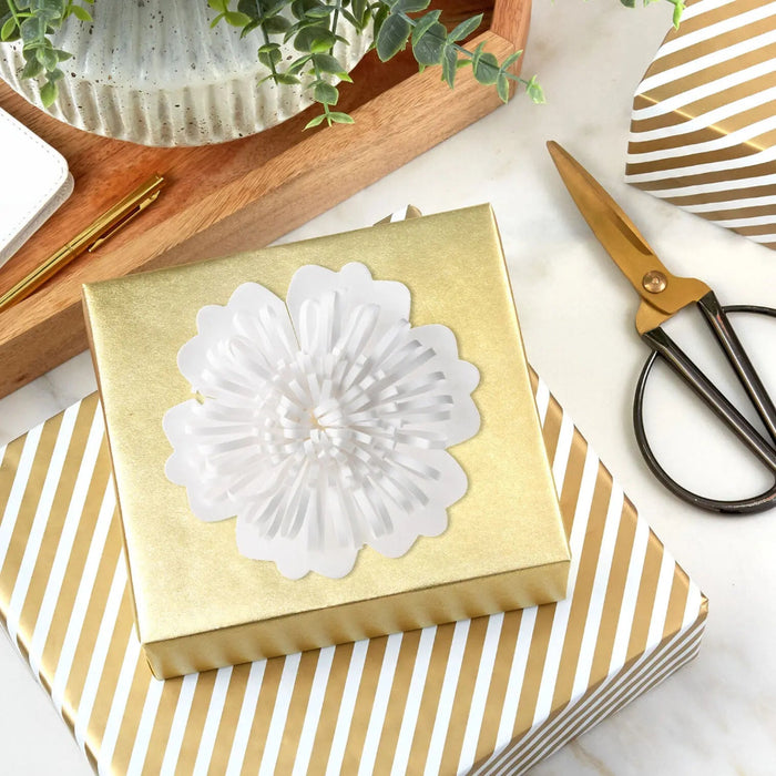 Cream‑colored flower bow with scalloped petals displayed on a gold present 