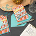Two 'Thanks' cards on a table with an envelope, pen, and notebook.