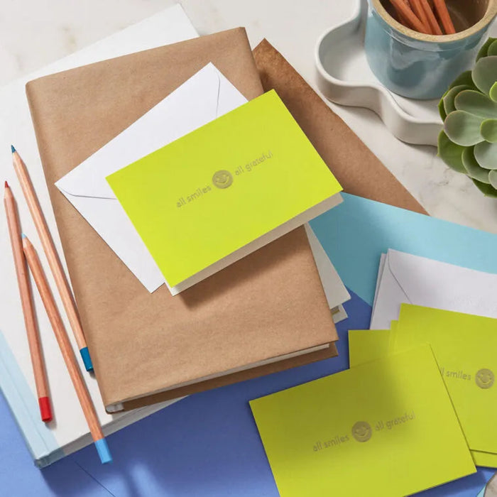 Notebooks, envelopes, and stationery items on a desk with a plant in the background.