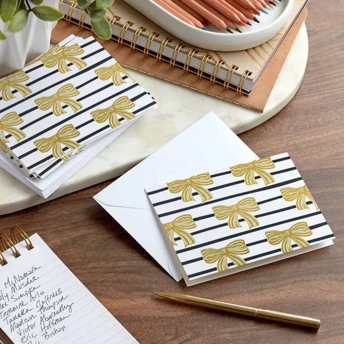 Notebooks with gold bow and black stripe design on a wooden surface with a pen.