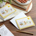 Set of greeting cards with animal illustrations on a wooden surface with stationery items.