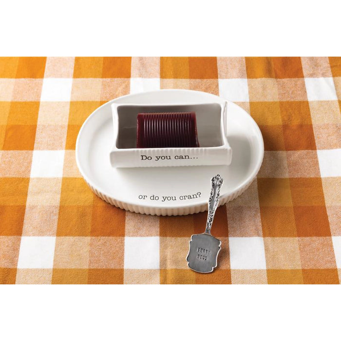 Cranberry sauce displayed in ceramic dish on plaid tablecloth.