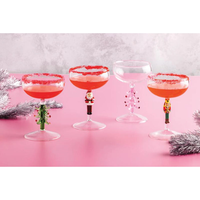 Four cocktail glasses with red drinks on a pink surface, surrounded by festive decorations.