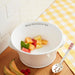 A white bowl containing ripe strawberries with a stainless steel spoon resting next to it.
