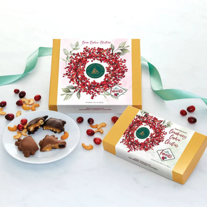 Harbor Sweets milk chocolate Cran Cashew Clusters, 5-piece box with golden-yellow ends and a white sleeve featuring a red cranberry wreath and green Harbor Sweets seal.