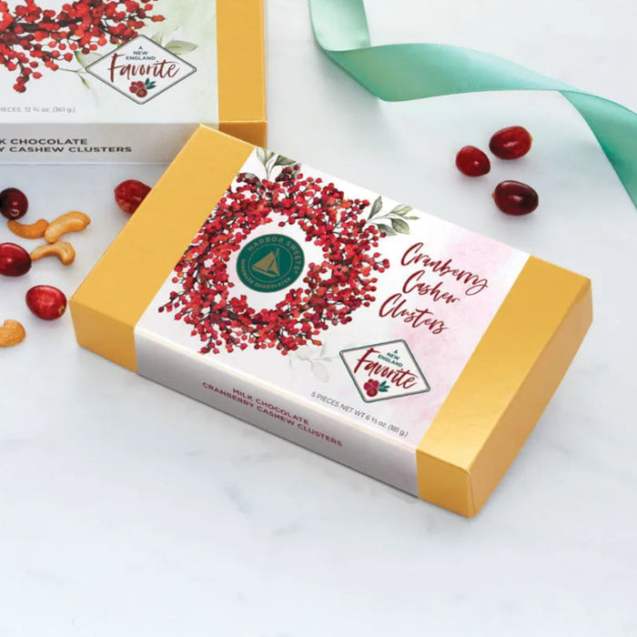 Harbor Sweets milk chocolate Cran Cashew Clusters, 5-piece box with golden-yellow ends and a white sleeve featuring a red cranberry wreath and green Harbor Sweets seal.