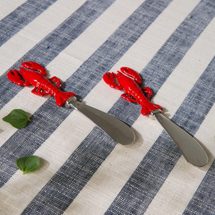 Two lobster-shaped red cutlery items are placed on a striped tablecloth, creating a whimsical dining atmosphere.