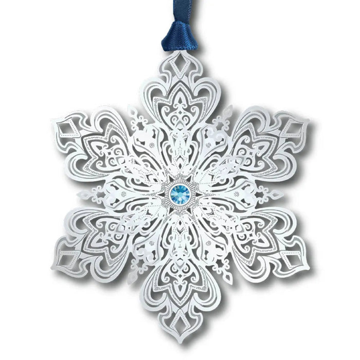 Decorative snowflake ornament with intricate patterns and a blue gem in the center, hanging from a blue ribbon on a white background.