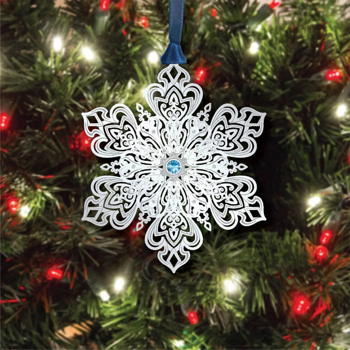 Decorative snowflake ornament with blue gem on a Christmas tree.