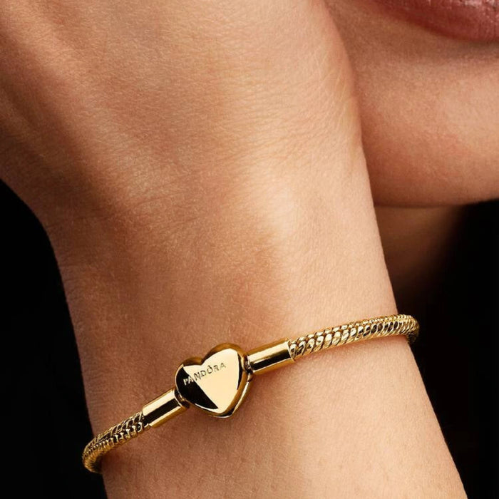 Gold-tone herringbone snake chain bracelet with a polished heart-shaped clasp designed for everyday wear and compatible with charms.